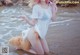 A woman in a white shirt and orange bikini sitting in the water.