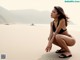 A woman in a black bikini sitting on a beach.