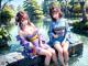 A couple of women sitting on top of a rock next to a pond.