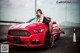 A woman leaning on the hood of a red sports car.