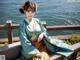 A woman in a blue and yellow hanbok sitting on a bench by the water.