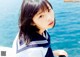 A young woman in a sailor outfit sitting by the water.